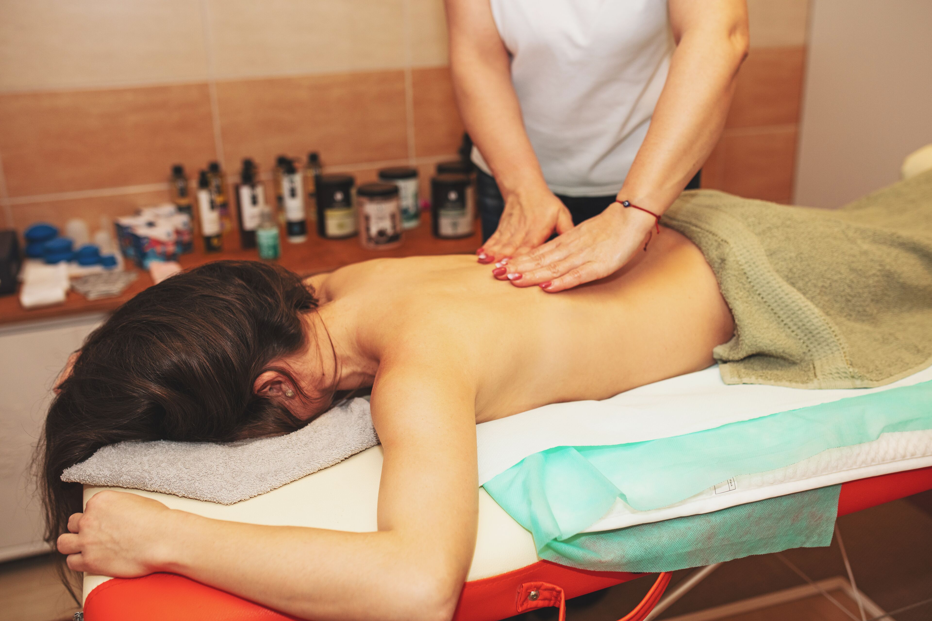 A massage therapy session in a room with a tiled wall and various bottles in the background.
