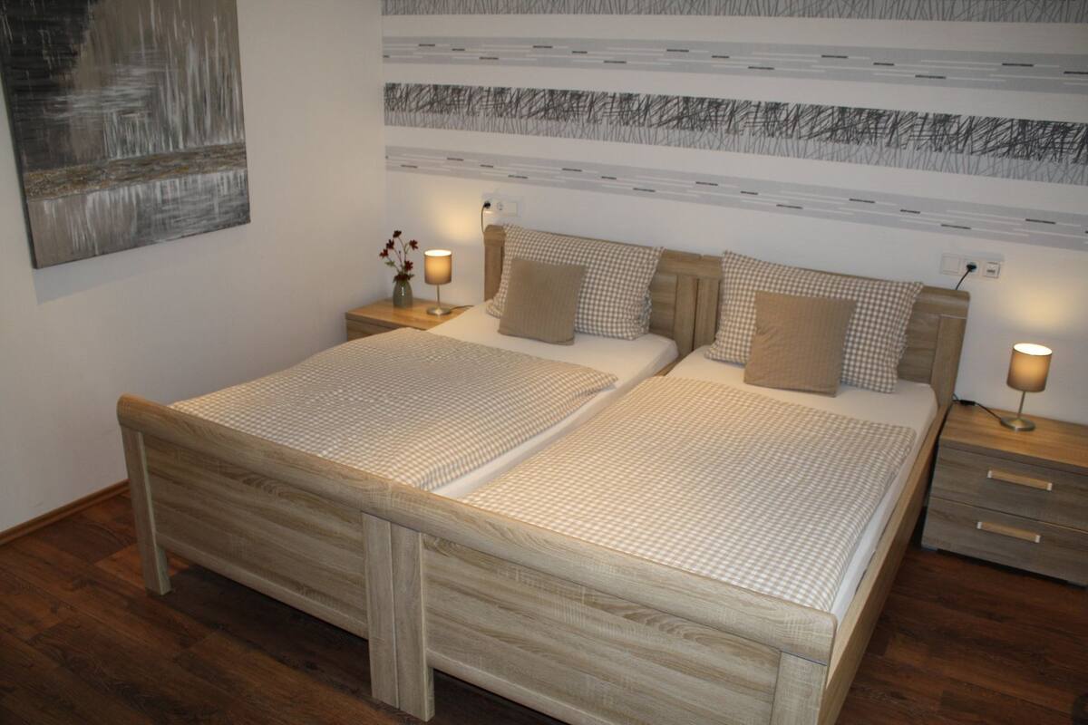 A double bed with a wooden frame, two bedside tables with lamps, a wall-mounted artwork, and a patterned wall above the bed.