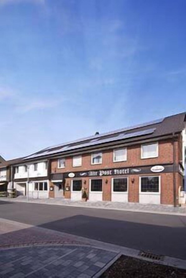 A two-story building with a sign reading "The Post Hotel." It has a brick facade, multiple windows, and a flat roof. - Alte Post Hotel (Schoeppingen)