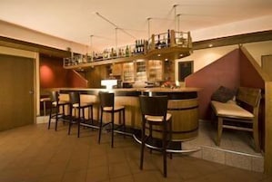 Una zona de bar con una barra alta, varios taburetes y un área de estar con un banco y sillas.