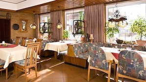 A restaurant with wooden furniture, brick walls, and large windows with plants. - Alte Post Hotel (Schoeppingen)