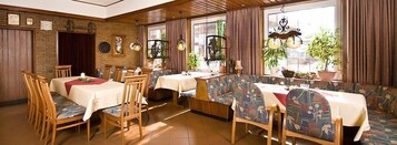 Un restaurante con mobiliario de madera, paredes de ladrillo y ventanas amplias con plantas.