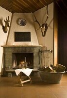 Un interior rústico con chimenea de piedra, cabeza de ciervo montada en la pared y una mesa de madera tosca.