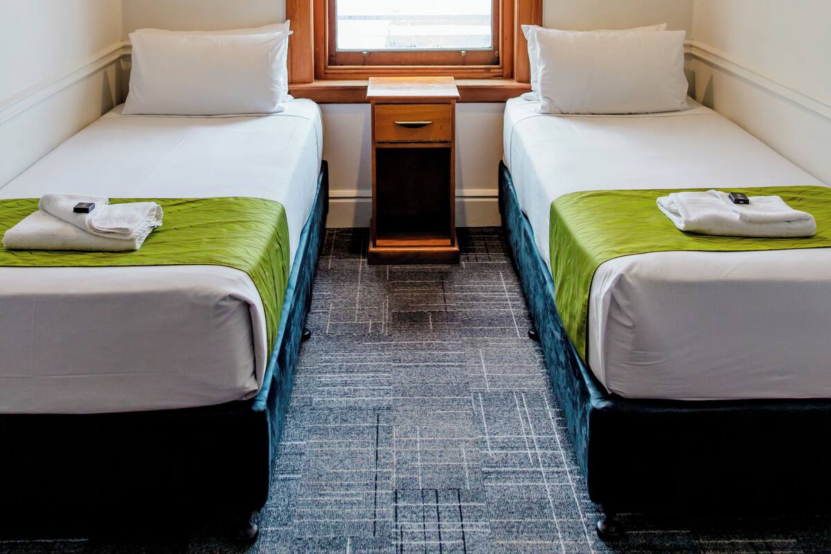 Habitación de hotel con dos camas, una ventana con marco de madera, una mesita pequeña y una lámpara colgante.