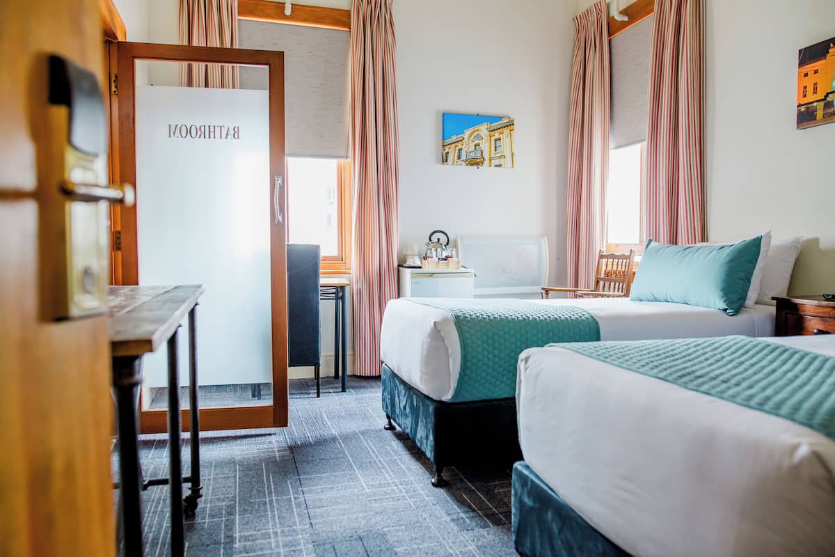 Habitación de hotel con dos camas, un escritorio, una silla, una mesita y una puerta con la etiqueta 'ROOM'.
