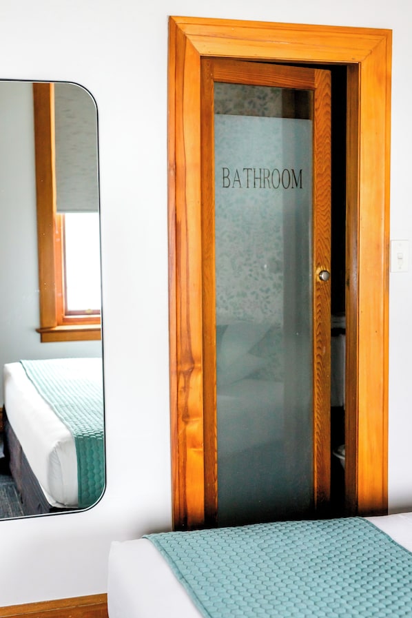 A bedroom with a bed, a mirror, and a door labeled "BATHROOM". - The Cambridge Hotel & Backpackers (Wellington)