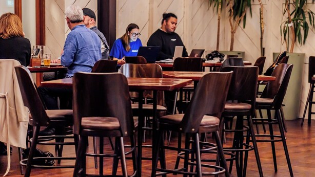 A restaurant with wooden beams and hanging paper lanterns. Tables are arranged with chairs, and people are dining. - The Cambridge Hotel & Backpackers (Wellington)