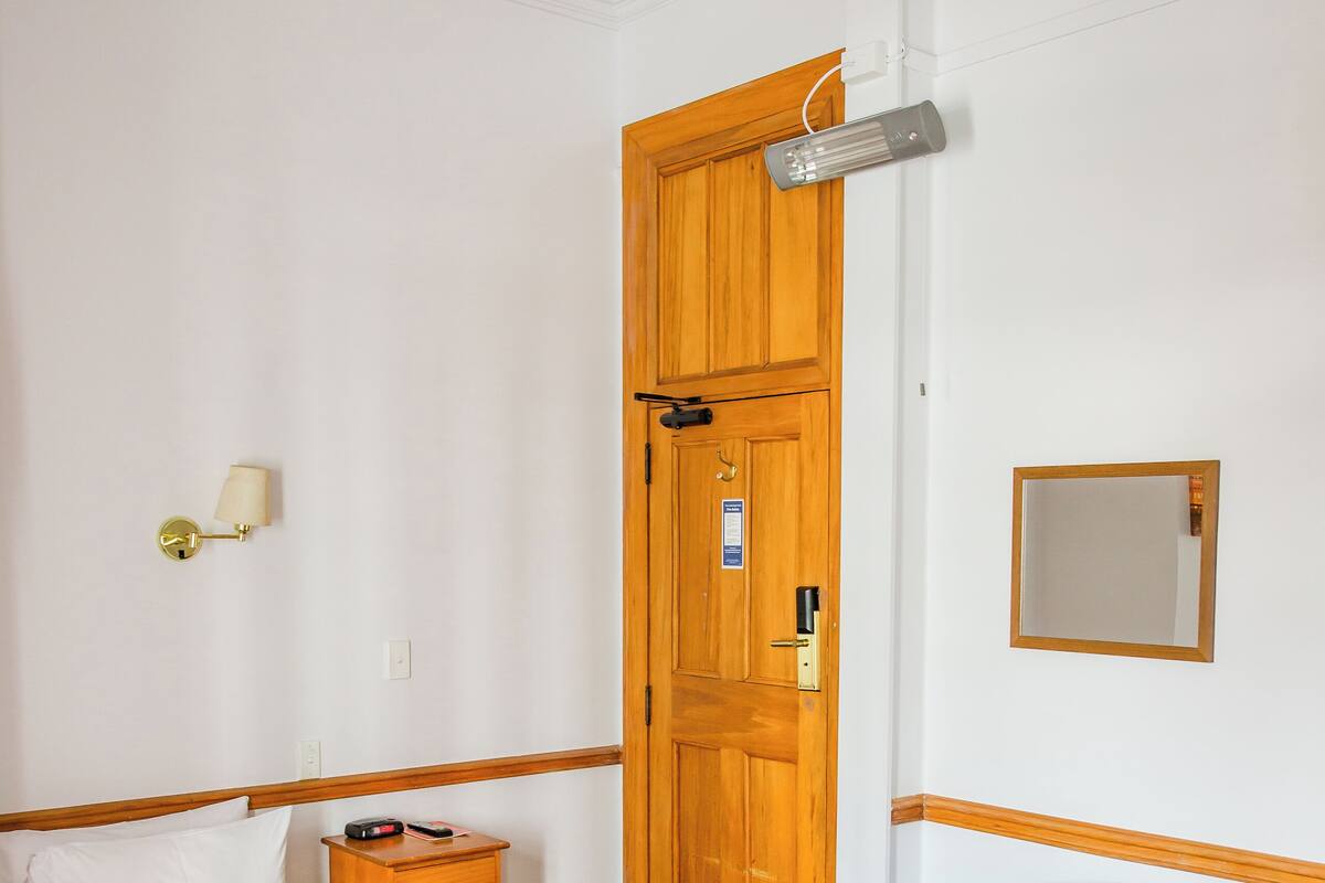 Una habitación de hotel con cama, sillón, mesita de noche, lámpara, espejo y puerta.