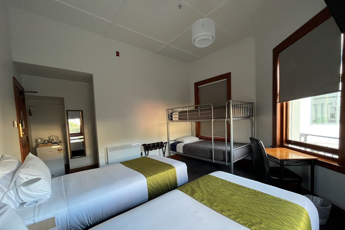 Habitación de hotel con dos camas, un escritorio, una silla, un espejo y una ventana con vistas.