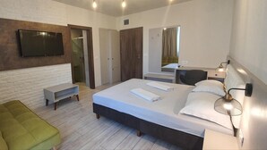 A modern hotel room with a large bed, a TV mounted on a brick wall, a seating area with a bench, and a mirror above the bed. - XO Residence (Arad)