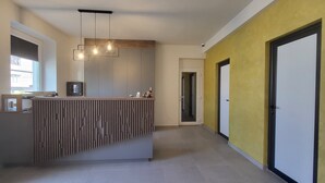 A reception area with a wooden reception desk, a modern pendant light fixture, and a view of the hallway. - XO Residence (Arad)