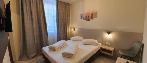 Una habitación de hotel con una cama, una silla, un escritorio y un televisor montado en la pared.