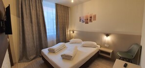 Una habitación de hotel con una cama, una silla, un escritorio y un televisor montado en la pared.