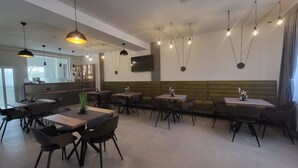 A restaurant with multiple tables and chairs, a bar area, and hanging pendant lights. - XO Residence (Arad)