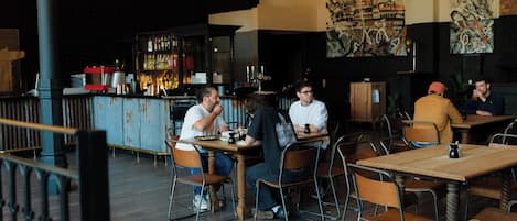 A restaurant with wooden tables and chairs, a bar area with bottles and glasses, and artwork on the walls.