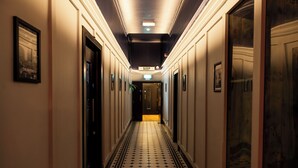 En hotellkorridor med ett klinkergolv, inramade tavlor på väggarna och dörrar som leder till rummen.