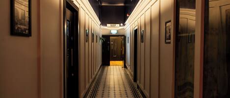 Un pasillo de hotel con suelo de baldosas, cuadros en las paredes y puertas que dan a las habitaciones.