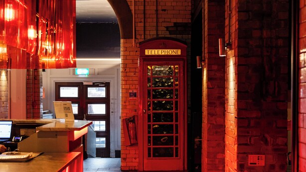 En hotellobby med en incheckningsdisk, en röd telefonkiosk och en receptionsdisk.
