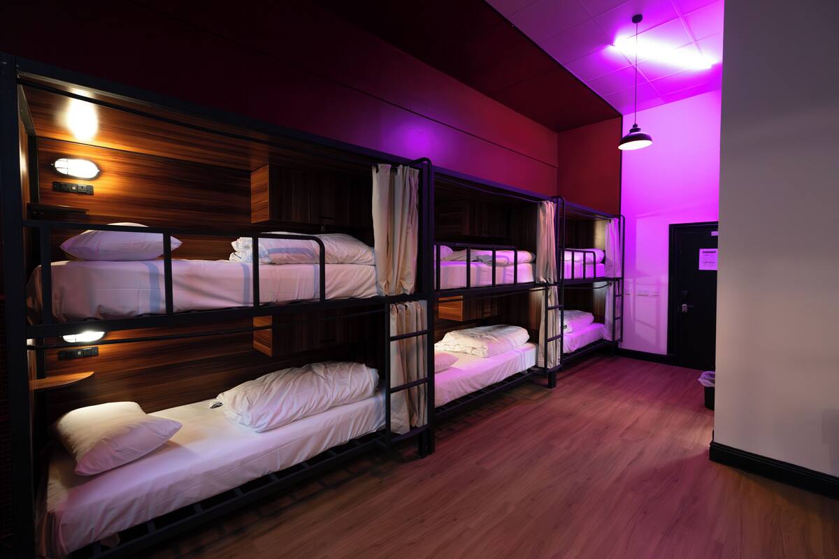 A room with bunk beds, wooden flooring, and purple ambient lighting.