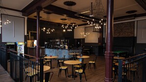 En restaurang med en inredning som inkluderar flera runda bord och stolar, en bardisk och en scen med en skärm.