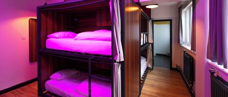 A bunk bed room with a wooden floor and a window on the right.