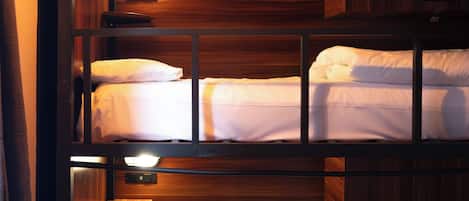 A bunk bed room with wooden paneling and a single bedside table.
