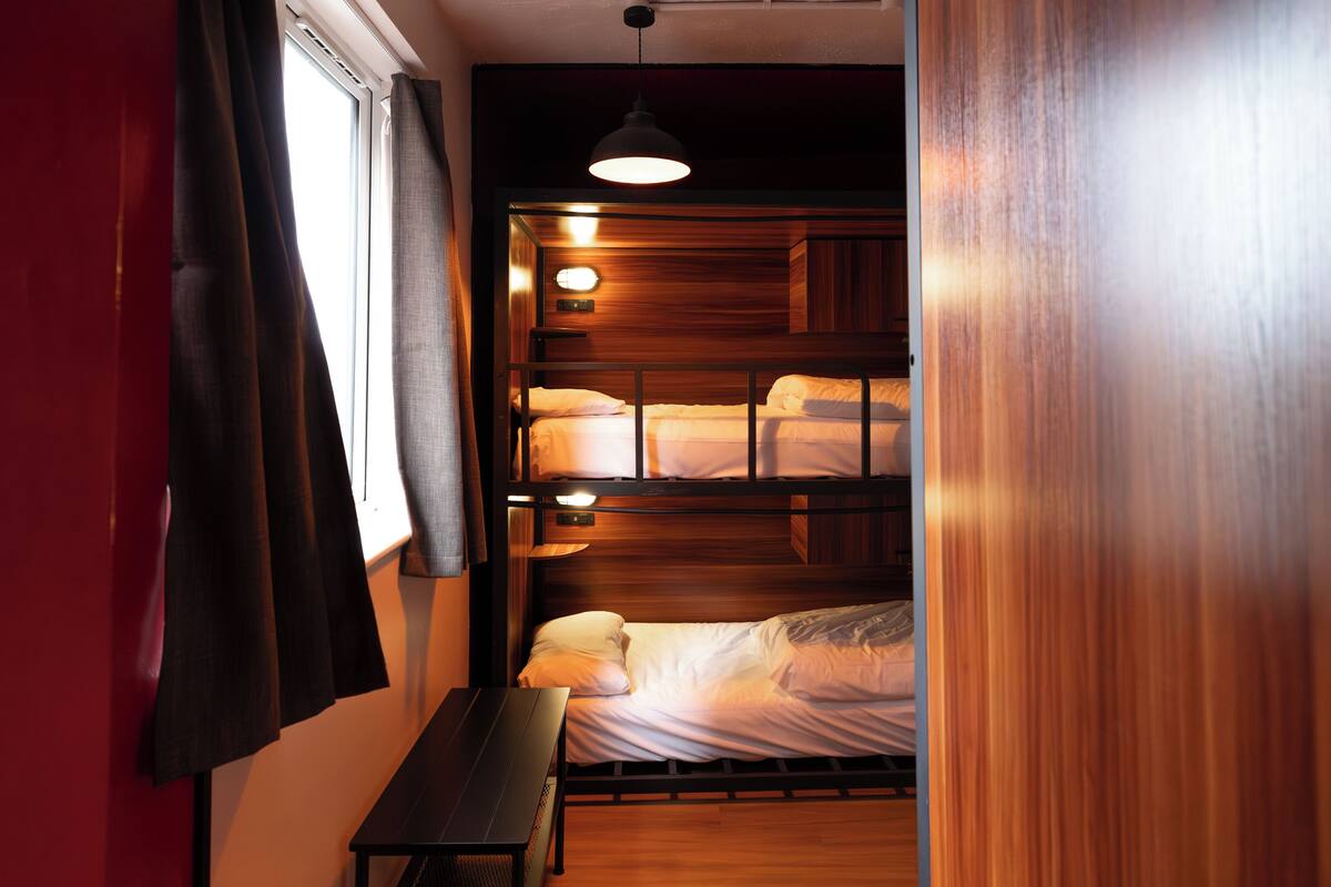 A bunk bed room with a wooden headboard, a small table, and a hanging light fixture.