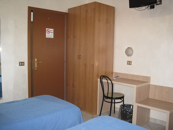 Une chambre avec deux lits, une armoire en bois, un bureau avec une chaise et un téléviseur fixé au mur.