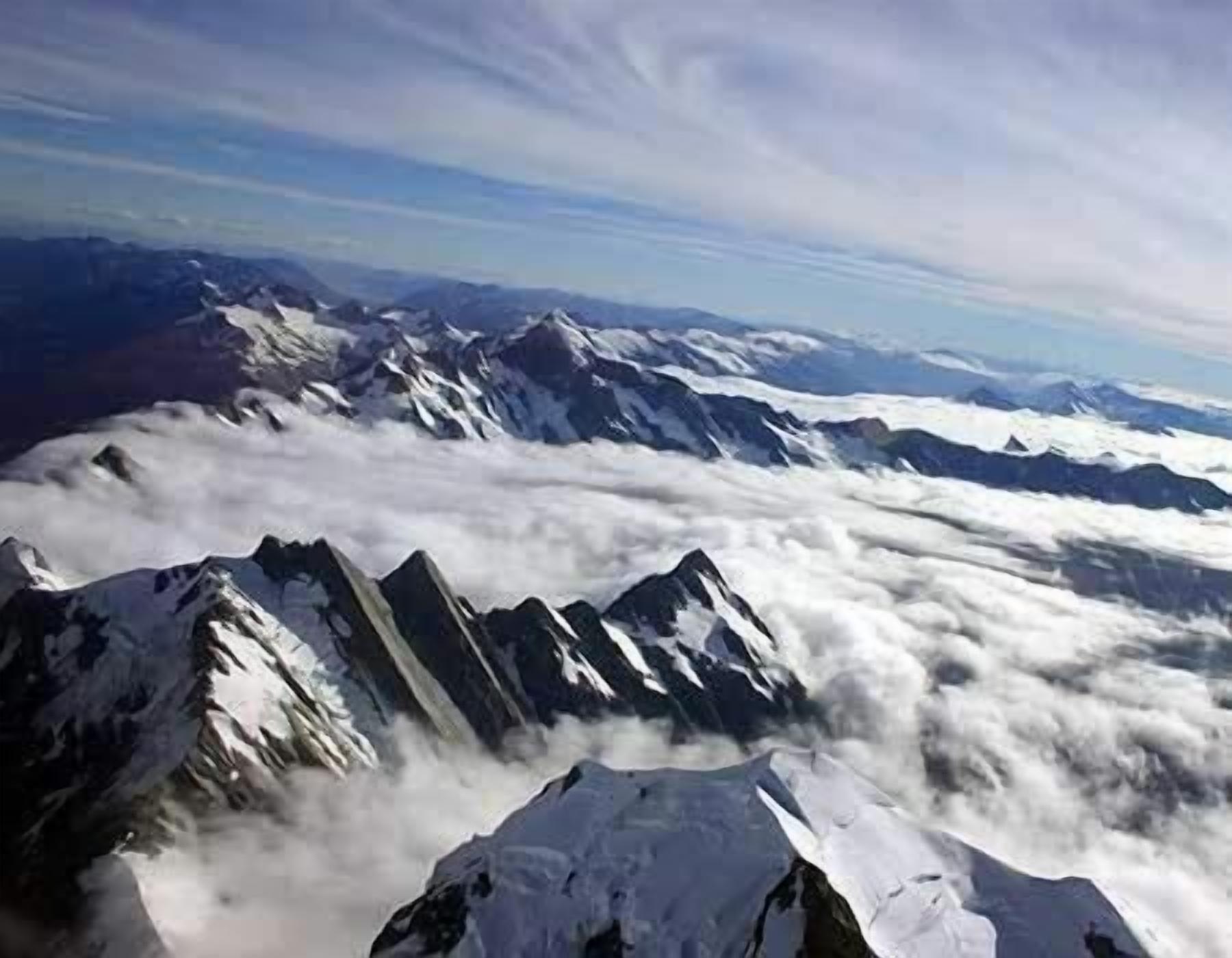 Un paisaje montañoso con picos nevados y una capa de nubes abajo.