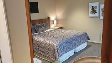 A bedroom with a bed, a nightstand, a wall-mounted lamp, and a mirror reflecting the room.
