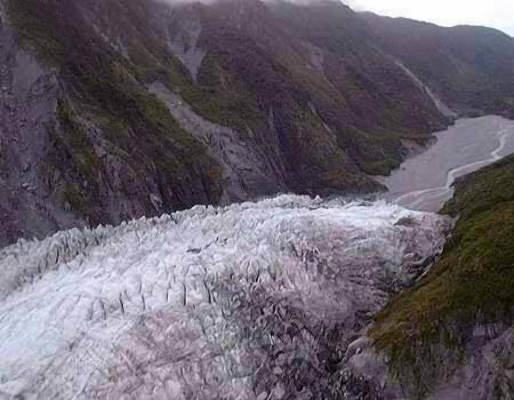 Un glaciar con un río que lo atraviesa, rodeado de terreno rocoso.