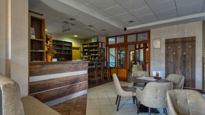 A restaurant with a wooden reception desk, bar area, and several cushioned chairs. - Garni Hotel Zvon (Zrece)