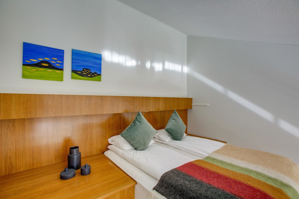 Una cama bien hecha con un edredón a rayas, un cabecero de madera y dos cuadros en la pared.