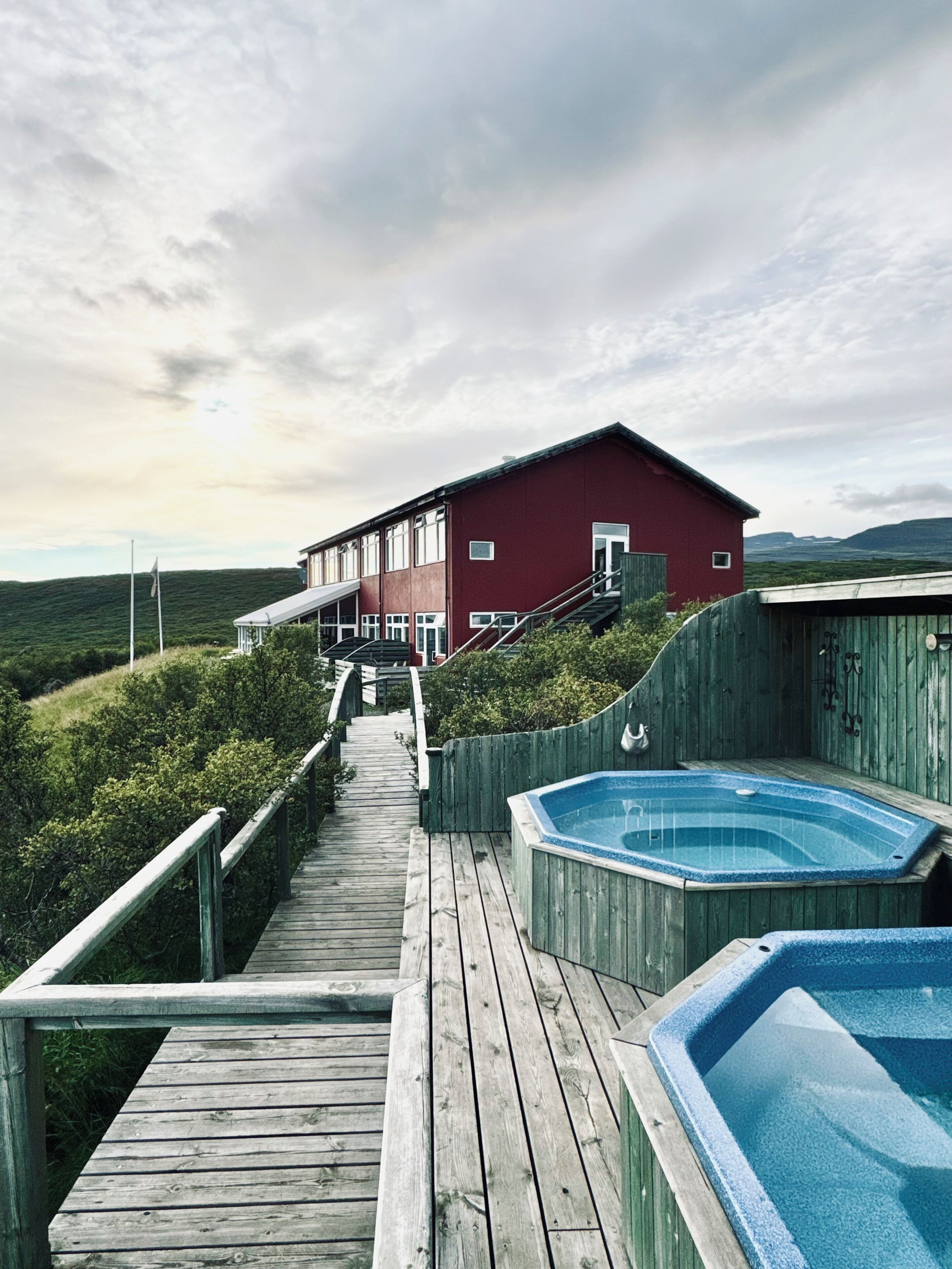 A wooden deck leading to a red building with a hot tub and a view of the landscape.