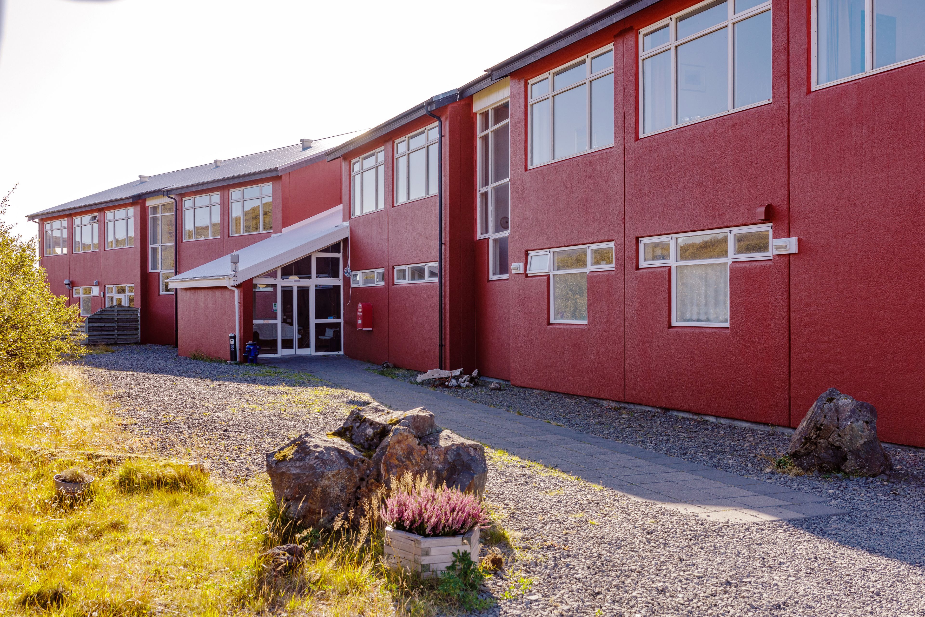Een rood gebouw met een overdekte ingang, grote ramen en een grindpad.