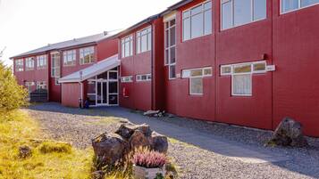 Een rood gebouw met een overdekte ingang, grote ramen en een grindpad.