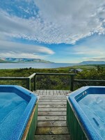 Una terraza de madera que conduce a un área de hidromasaje con vistas a un lago y montañas distantes.