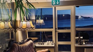 A cozy room with a plush sofa, a large plant, and a view of the sea through a glass door. - Hotel Glymur (Hvalfjarðarsveit)