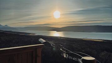 A wooden staircase leading to a viewing platform overlooking a body of water and distant mountains during sunset.