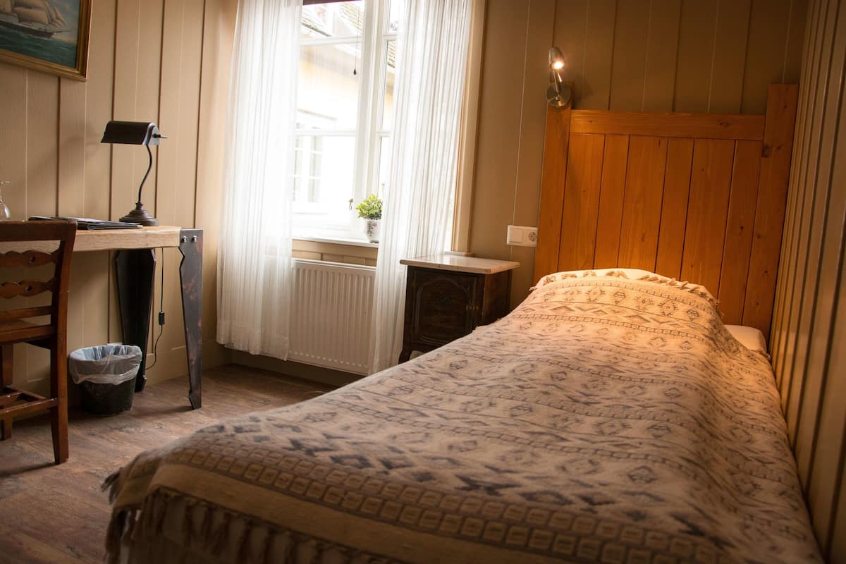 Ein Schlafzimmer mit einem Holzkopfteil, einem Schreibtisch mit Lampe, einem Heizkörper und einem Fenster mit Vorhängen.