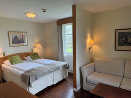 Habitación de hotel con dos camas, un sofá y una mesa. Incluye lámparas de pared y una ventana con cortinas.