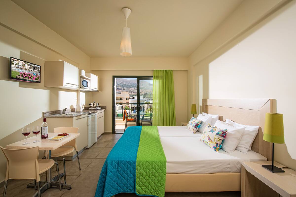 A hotel room with a bed, a desk, a kitchenette, and a balcony with a view.
