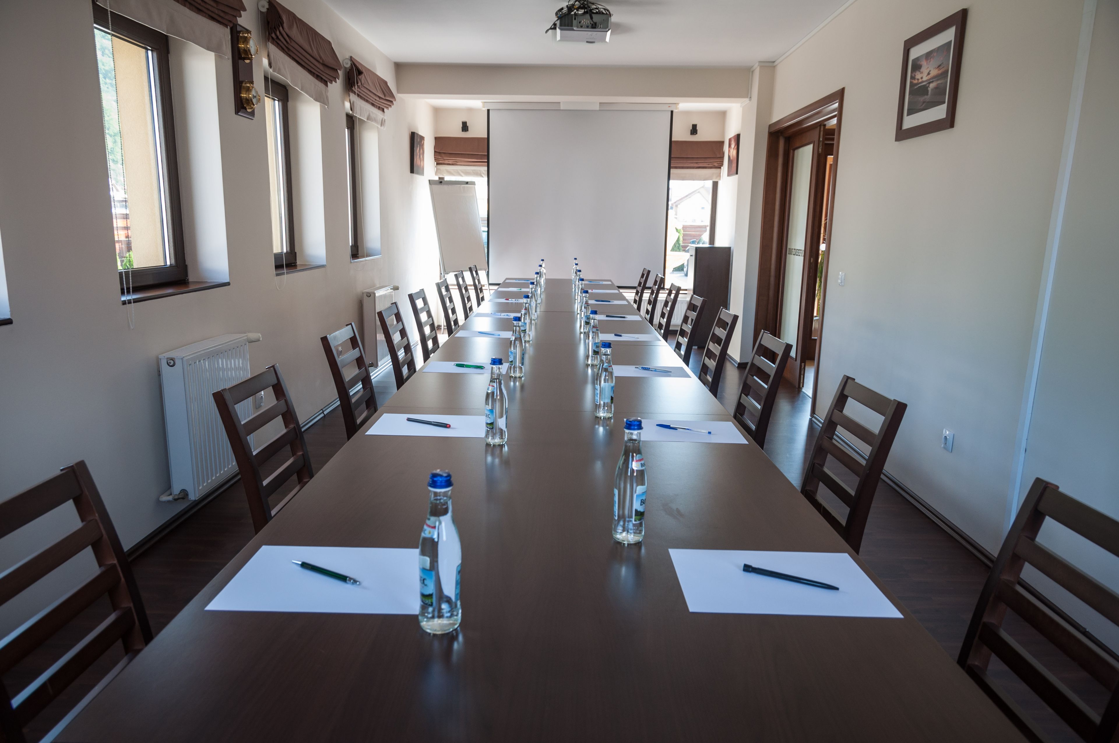 Un salón de conferencias con una larga mesa, sillas, botellas de agua y documentos.