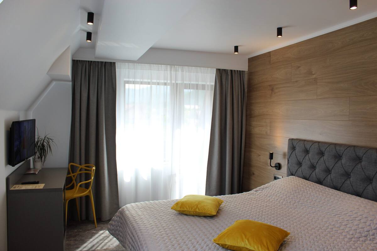 A modern hotel room with a large bed, a desk, a chair, and a television.