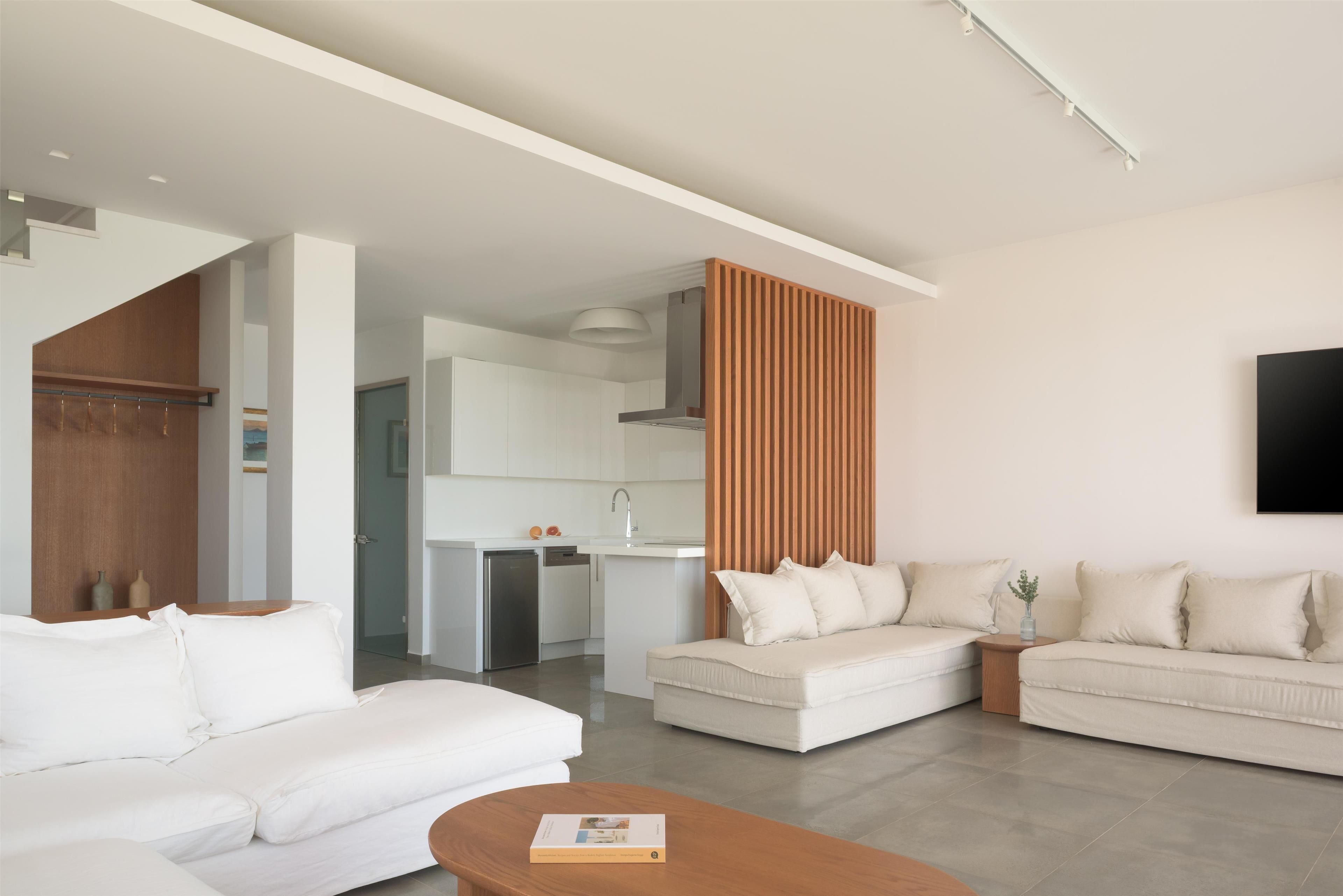 A modern living room with a white sofa set, a wooden coffee table, and a kitchen in the background.
