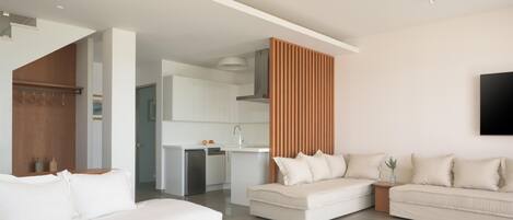 A modern living room with a white sofa set, a wooden coffee table, and a kitchen in the background.