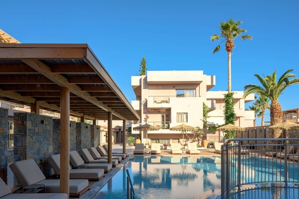 A poolside area with lounge chairs, a pool, and a building with balconies and palm trees.