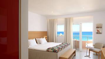 A hotel room with a bed, a bench, a chair, a small table, and a view of the sea through large windows.