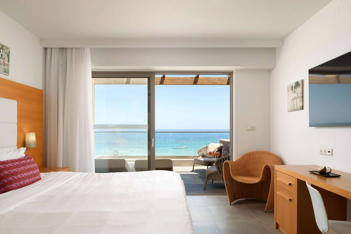A hotel room with a bed, a desk, a chair, and a view of the ocean.