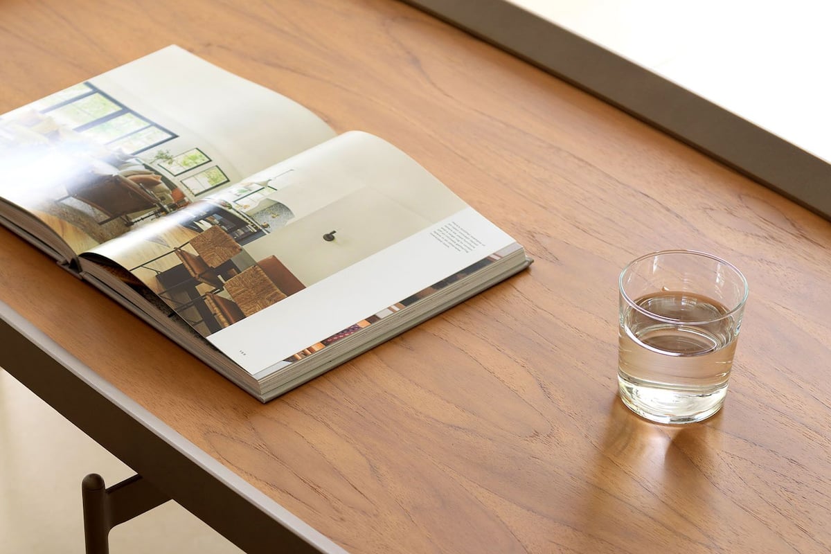 An open magazine on a wooden table with a clear glass of water beside it.